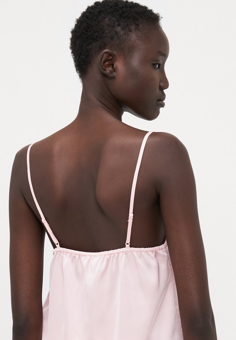 Camisola di seta rosa con spalline regolabili, caratterizzata da una vestibilità ampia e un orlo elastico arricciato, che mette in evidenza una texture liscia e lucida.