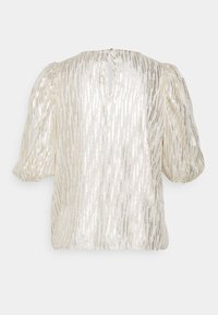 Blusa de mangas abullonadas en color crema con rayas metálicas. Presenta un escote tipo keyhole en la parte posterior y una tela texturizada. Diseño suave y ligero.