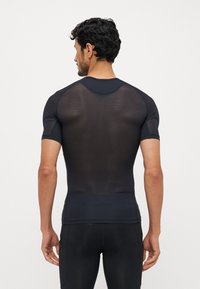 Schwarzes Sportshirt mit kurzen Ärmeln aus atmungsaktivem Mesh-Gewebe. Enganliegendes Design mit subtiler Textur und verstärkten Nähten am Kragen.