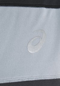 Tessuto atletico grigio con superficie testurizzata e rifiniture nere. Presenta un logo argento riflettente ben visibile.