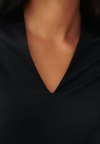 Black v-neck top featuring a smooth texture, with a deep neckline and subtle stitching detailing along the edges.