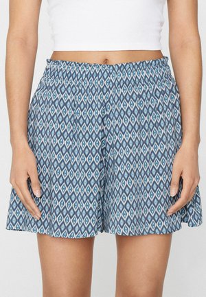 Femme portant un short ample à motif losanges bleu et blanc avec une taille élastique et un débardeur court blanc.