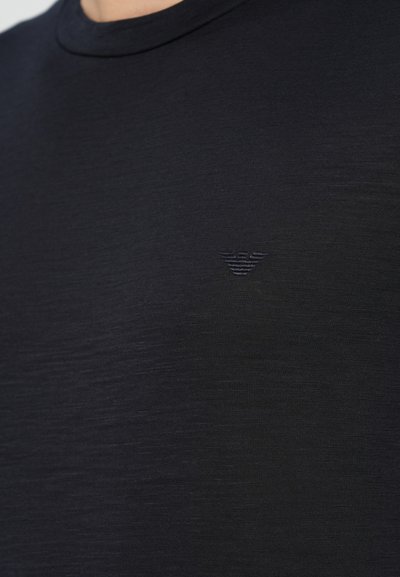 Fekete, rövid ujjú póló kerek nyakkivágással, texturált anyagból. Bal mellrészen kis, tónusos logóval díszítve.