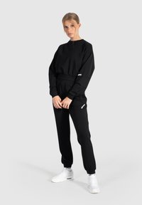 Zwarte twee-delige sportoutfit met een cropped sweatshirt met lange mouwen en joggers met elastische tailleband, aangevuld met witte sneakers.