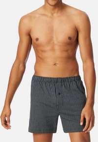 Boxers bleu marine avec des rayures verticales blanches, fabriqués à partir d'un tissu léger. Taille élastique avec un bouton à l'avant.