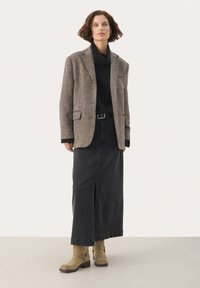 Pruun houndstooth mustri bleiser, must turtleneck, põlvepikkune must seelik lõhiku jaotusega, beežid pahkluu saapad klambritega, ühetooniline taust.