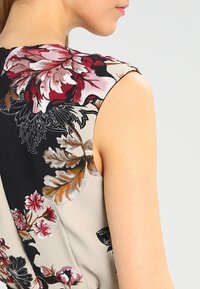 Blomstermönstrad topp i lätt tyg, med röda och svarta blommor. Designen kompletteras av beige och mjuka gröna accenter.