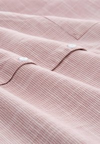 Pink and white small checkered fabric with two white buttons on folded shirt cuffs, showing texture and stitching details.