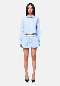 Blau-weißer gestreifter, kurz geschnittener Shirt mit langen Ärmeln, kombiniert mit einem passenden Rock mit Kordelzug. Schwarze High Heels runden das Outfit ab.