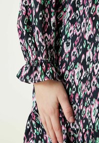 Czarna sukienka z tkaniny z kolorowym abstrakcyjnym wzorem w odcieniach różu, zieleni i bieli. Charakteryzuje się zgromadzonymi rękawami z falbankami oraz luźnym krojem.