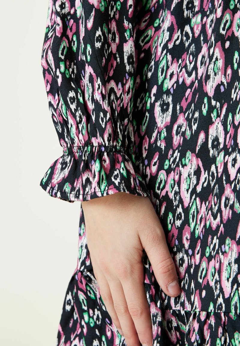 Czarna sukienka z tkaniny z kolorowym abstrakcyjnym wzorem w odcieniach różu, zieleni i bieli. Charakteryzuje się zgromadzonymi rękawami z falbankami oraz luźnym krojem.