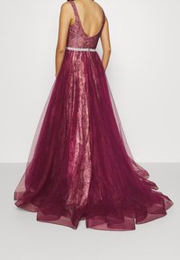 Burgundowa wieczorowa sukienka z koronką, z dopasowanym gorsetem, dekoltem w kształcie litery V na plecach oraz warstwową spódnicą z tiulu. Posiada beadedowy pas i kwiatowe wzory.