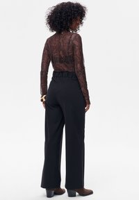 Przeźroczysta czarna bluzka z długim rękawem z wzorem wężowej skóry, zestawiona z czarnymi spodnimi o wysokim stanie, z marszczonym paskiem i szerokimi nogawkami.