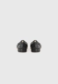 Chaussures plates en cuir noir avec un bout arrondi, texture douce et design minimaliste ; dotées d'un petit accent métallique à l'arrière.