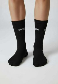 Zwarte geribbelde sokken met de tekst "SIXTH JUNE" in het wit gedrukt op het bovenste deel. Enkellang ontwerp met een nauwsluitende pasvorm. Zachte textuur.