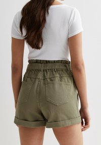 Shorts verde oliva con una vita alta elasticizzata e dettagli arruffati. Presentano risvolti e due tasche posteriori. Il tessuto è strutturato.