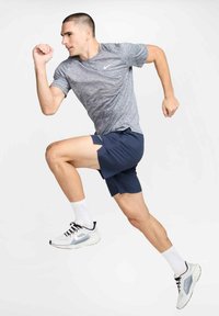 Conjunto deportivo que incluye una camiseta gris texturizada, pantalones cortos azul marino con aberturas laterales y zapatillas blancas con detalles en negro.