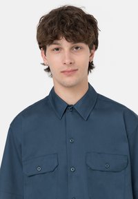 Camicia blu scuro a maniche corte realizzata in tessuto morbido, con colletto classico, due tasche sul petto e chiusura frontale con bottoni.
