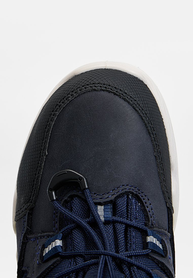 Nahaufnahme einer marineblauen Sneaker-Spitze mit weißer Sohle, einer schwarzen strukturierten Zehenkappe und elastischen Schnürsenkeln, die von einem Kunststoffschloss gehalten werden.