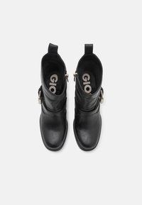 Botas de tobillo de cuero negro con textura suave, que cuentan con cremalleras laterales y correas ajustables. Diseño de punta redonda y altura corta.