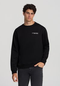 Felpa nera in misto cotone, con collo rotondo, maniche lunghe e una piccola scritta logo stampata in bianco sul davanti.