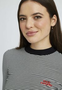 T-shirt à rayures noires et blanches à manches longues avec un col rond. Présente un texte brodé rouge "Profitez de chaque jour" sur la poitrine. Texture de tissu lisse.