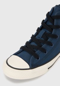 Baskets montantes en toile navy avec lacets noirs, capuchon en caoutchouc et semelle texturée. Présente un design classique avec des accents blancs contrastants.