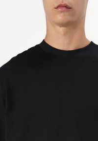 T-shirt nera in cotone con un morbido texture. Maniche corte, finitura liscia e senza motivi o grafiche visibili.