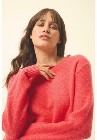 Heller Korallpullover aus weichem, strukturiertem Strick mit gerippten Bündchen und weitem Ausschnitt, in lässiger Passform und entspannter Drapierung.