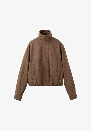 Chaqueta marrón de cuello alto con lunares negros, dobladillo elástico, mangas largas y bolsillos delanteros sobre fondo blanco.