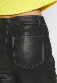 Svarta läderbyxor med vit sömdetalj på bakfickan, bärs med en kort ärmad gul ribbad tröja.