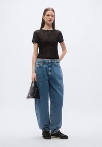 Juoda dryžuota tinklelinė marškinėliai, mėlyni laisvi džinsai, juoda rankinė ir juodi sportbačiai su šviesiomis detalėmis. Paprasta, moderni estetika.