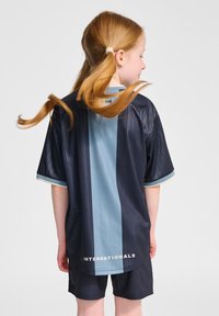 Marinblå sporttröja med ljusblå vertikal rand, korta ärmar och texten "INTERNATIONALS" på baksidan. Lättviktigt tyg, avslappnad passform.