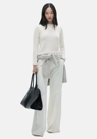 Maglione leggero crema con scollatura rotonda, cintura grigia attorno alla vita, pantaloni bianchi a gamba larga e una borsa nera a tracolla con forma strutturata.