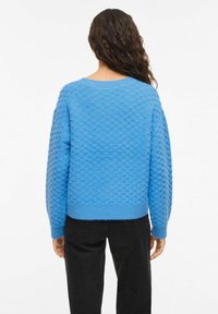 Pull en maille texturée bleue avec un col rond, des manches longues et un ourlet côtelé. Matière en mélange de coton avec une apparence douce et duveteuse.