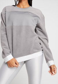 Grå fleece sweatshirt med skinnende sølv accenter, med rund halsudskæring og sideskydder for nem bevægelse.