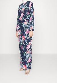 Długa sukienka maxi w kwiatowy wzór na granatowym tle, z długimi rękawami oraz żywymi różowymi, zielonymi i niebieskimi motywami; lekka tkanina i luźny krój.