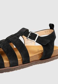 Schwarze Wildleder-Sandale mit mehreren breiten Riemen, einer quadratischen silbernen Schnalle und einer Korksohle mit strukturiertem Oberfläche.