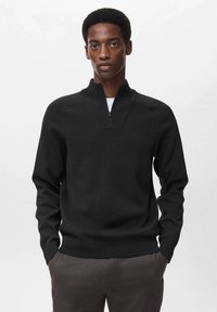 Maglione nero a maglia con collare a mezza zip, caratterizzato da una finitura testurizzata e polsini aderenti, indossato sopra una t-shirt bianca. Sfondo semplice.