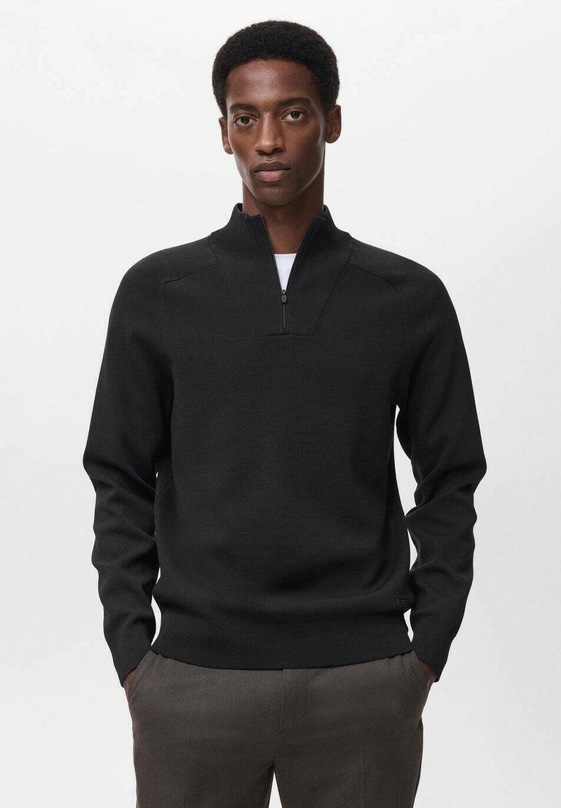Maglione nero a maglia con collare a mezza zip, caratterizzato da una finitura testurizzata e polsini aderenti, indossato sopra una t-shirt bianca. Sfondo semplice.