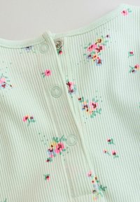 Svetlozelená rebrovaná tkanina s malými ružovými a červenými kvetinovými vzormi, s patentkami pozdĺž stredového švu.