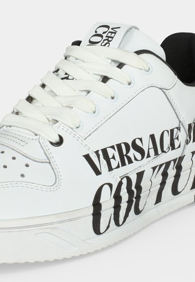 Бяла кожена маратонка с бели връзки и черен "VERSACE JEANS COUTURE" надпис отстрани и на езица, с черен вътрешен подплатен слой.