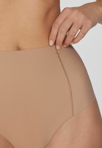 Beige, hoge taille onderbroek gemaakt van glad, rekbaar materiaal met een naaddetail langs de tailleband en beenopeningen.