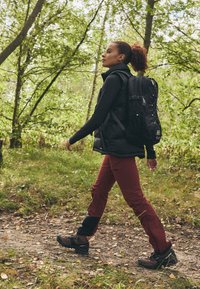 Black puffy vest over a long-sleeve top, burgundy pants with black accents, and brown hiking boots; carrying a black backpack, walking outdoors.