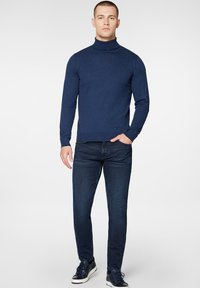 Granatowy sweter z golfem wykonany z gładkiej dzianiny, dopasowany krój, zestawiony z ciemnoniebieskimi dżinsami i casualowymi trampkami z białą podeszwą.