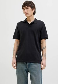 Polo shirt nero a maniche corte con colletto, realizzato in tessuto morbido. Presenta una vestibilità rilassata, cuciture sottili e una classica patta a due bottoni.