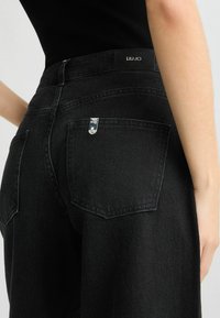 Jeans neri in denim a vita alta, con due tasche posteriori, accessori in argento e cinturino con logo. Tessuto testurizzato con una finitura pulita.