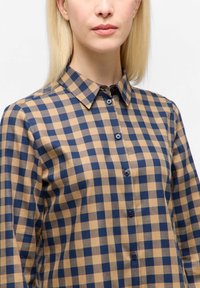 Button-up shirt featuring a plaid pattern in beige and navy. Made of a smooth fabric, with a classic collar and dark buttons.