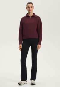 Pulover tricotat bordeaux cu guler înalt și fermoar pe jumătate, având un model texturat, asortat cu pantaloni negri ajustați și adidași luminoși.