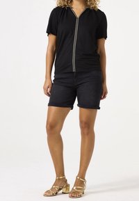 Czarna bluzka z krótkim rękawem, z wycięciem w kształcie litery V i ozdobnym przeszyciem. Do kompletu ciemne krótkie spodenki dżinsowe oraz złote sandały na słupku z paskami.